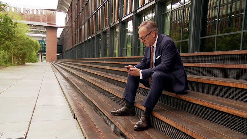 Prof. Dr. Klemens H. Fischer sitzt auf einer Treppe und schaut auf sein Handy